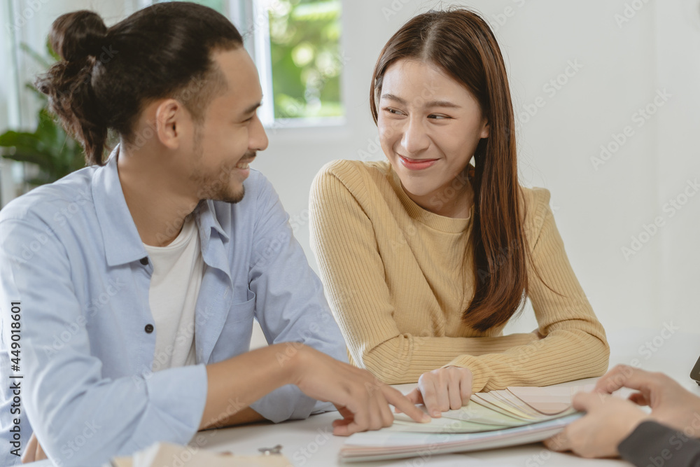 Happy asian couple client, people choose color on palette chart for swatch, paint on wall for new home with designer woman at office desk. Material of interior design. Happy asian couple client, people choose color on palette chart for swatch, paint on wall for new home with designer woman at office desk. Material of interior design.