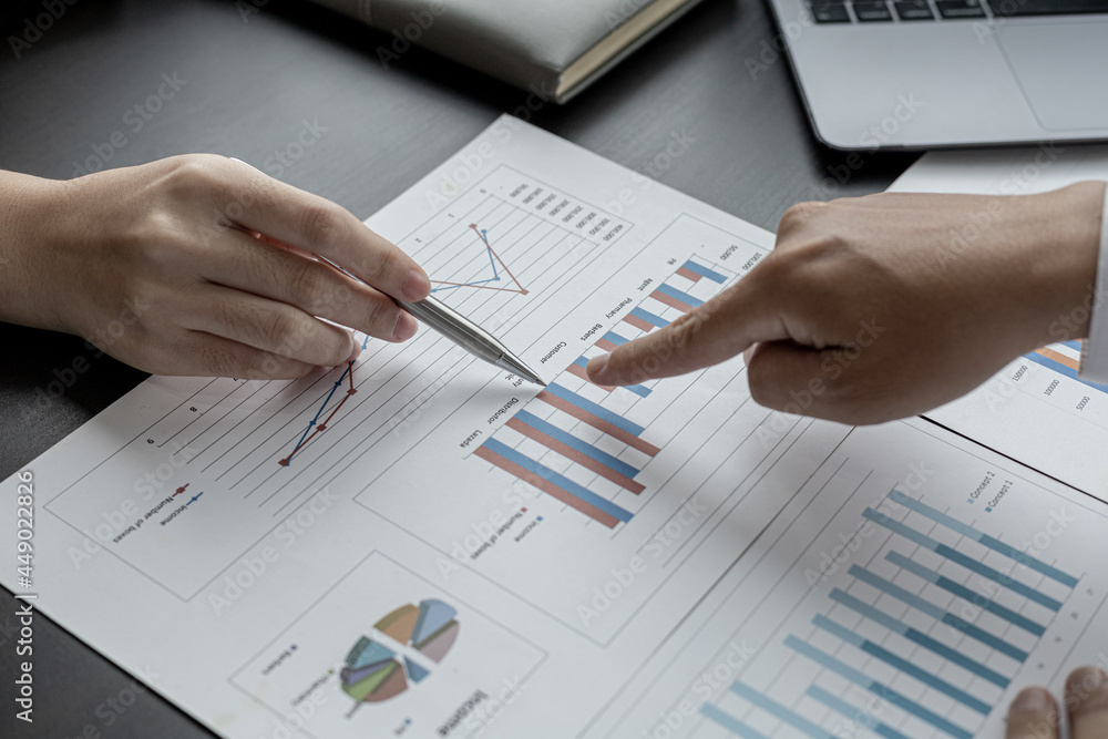Close-up photo of two businessmen pointing at a sales data sheet in graph format, they are meeting together on the topic of managing sales growth. Concept of business cooperation and sales management. Close-up photo of two businessmen pointing at a sales data sheet in graph format, they are meeting together on the topic of managing sales growth. Concept of business cooperation and sales management.