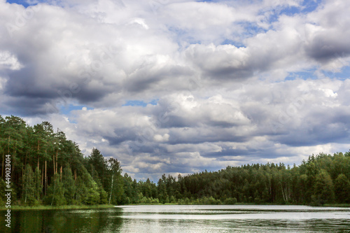 Beautiful cloudy sky over forest lake  summer landscape
