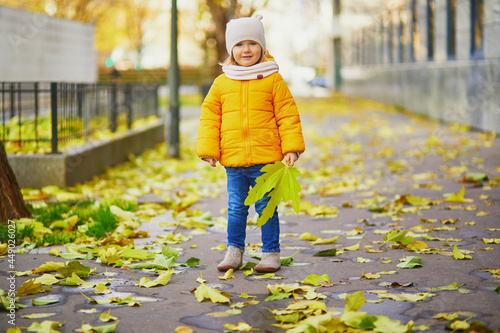 Adorable little girl in yellow jacket walking in autumn park on a sunny fall day