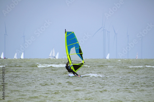 Young woman windsurfing with sailing boats and wind turbines at the horizon (Ijsselmeer, Netherlands) photo