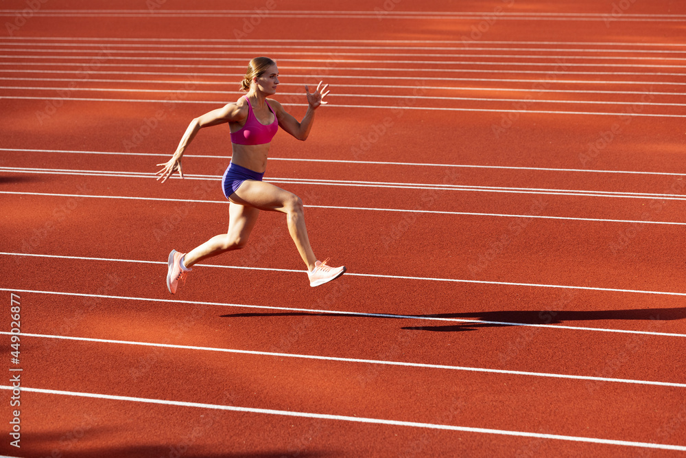 One Caucasian woman, female athlete, runner training at public stadium, sport court or palyground outdoors. Summer sport games.