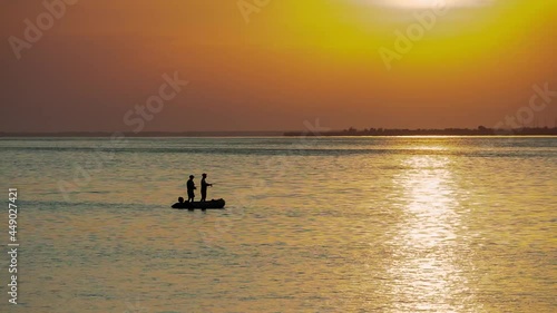 two fishermen on a boat fishing at sunrise