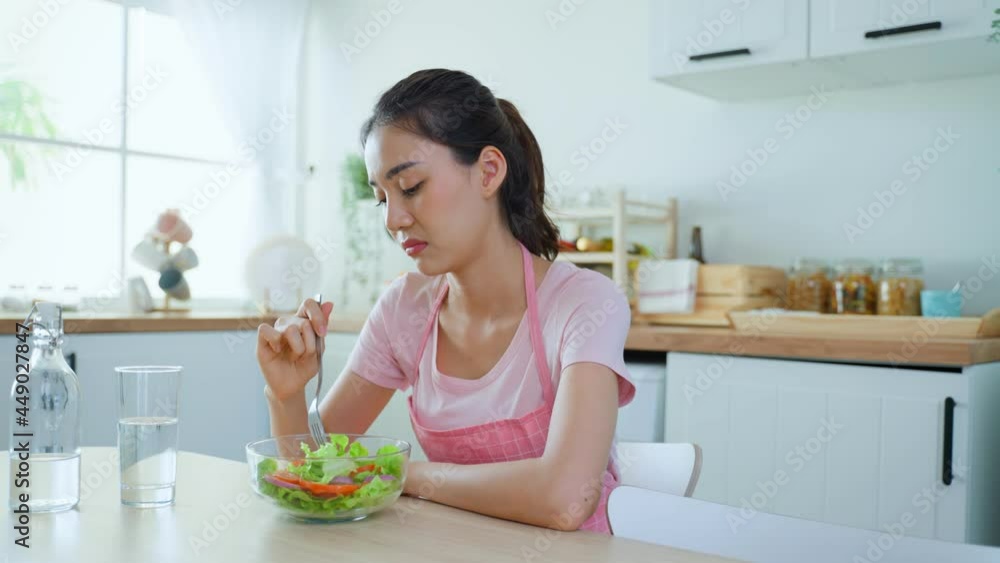 Asian attractive woman in apron don't want to eat green salad in house Asian attractive woman in apron don't want to eat green salad in house