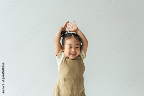 Leinwand Poster happy asian toddler girl with raised hands isolated on grey