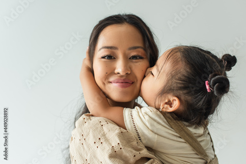 Fotografija asian toddler girl kissing cheek of happy mother isolated on grey