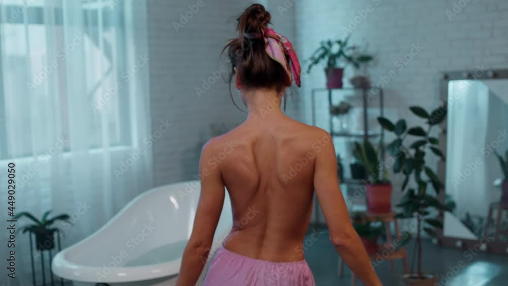 Taking video from the back beautiful lady take off the pyjama she walking to the bath to have a spa time she listen music from wireless headphones