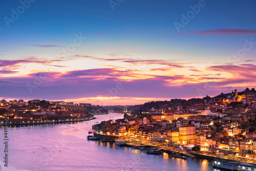 View from the Luis I Bridge of the Douro embankment at sunset, the city lit by lights, boats and houses along the coast.