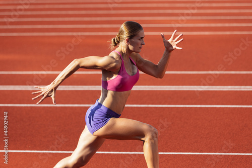 One Caucasian woman, female athlete, runner training at public stadium, sport court or palyground outdoors. Summer sport games.