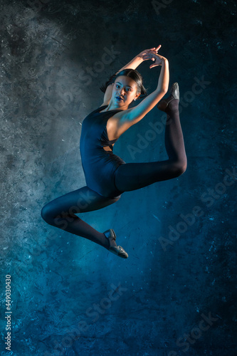 Fototapeta Naklejka Na Ścianę i Meble -  Dance and Gymnastics: Photograph of a young ballerina jumping in front of a textured background. girl making a demonstration of energy and vitality, in a powerful and stylized movement