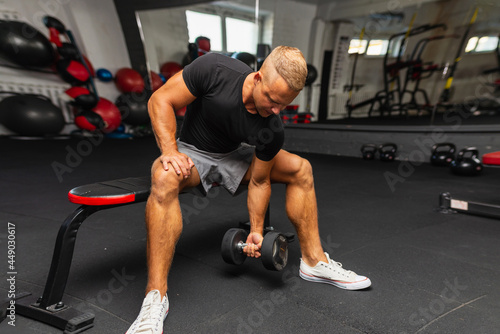 Young athlete Working out biceps at the gym.muscular young man lifting weights in gym on a dark background.Wide view © ARVD73