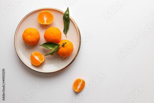 Fresh tangerine or clementin fruits on a beige plate with a gold rim on white background. Colorful fruit background. Flat lay, top view, copy space. Decorative christmas holiday composition photo