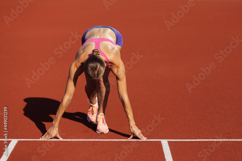 At start line. One Caucasian woman, female athlete, runner training at public stadium, sport court or palyground outdoors. Summer sport games. photo