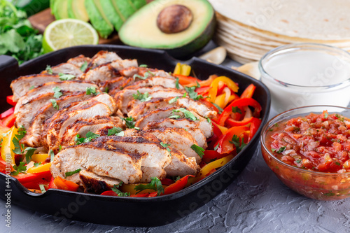 Chicken Fajitas with bell pepper and onion in a pan, served with salsa Asada, sour cream, avocado and tortillas, horizontal photo