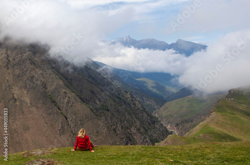 A woman in red sitting on a cliff, against a background of mountains. Mountain Digoria. North Ossetia. Russia. photo