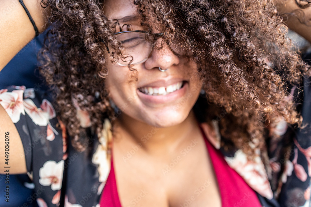 African American woman with long curly hair and glasses is happy and smiling at an outdoor park. it a cheerful afternoon with the sun touching her beautiful brown skin. African American woman with long curly hair and glasses is happy and smiling at an outdoor park. it a cheerful afternoon with the sun touching her beautiful brown skin.