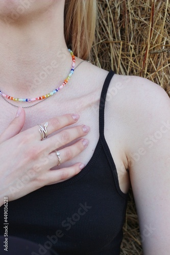 Body details of a beautiful young woman. Shoulder, collarbone and neck. A hand with rings touches the skin. Chain around the neck of multi-colored beads. Vertical photo