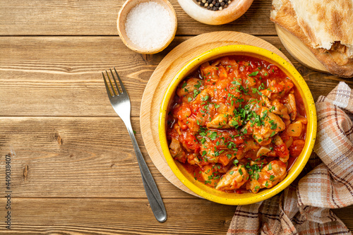 Traditional georgian dish Chakhokhbili. Chicken stew with tomatoes in ceramic bowl on wooden background.