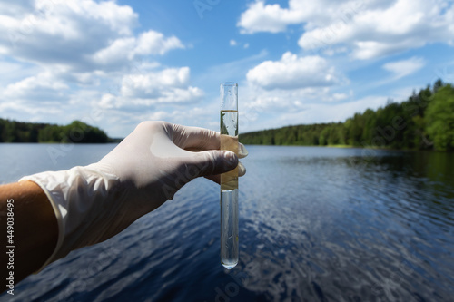 Scientist takes samples of dirty water from a pond. Hand is collects water in a test tube. Lake water pollution concept.
