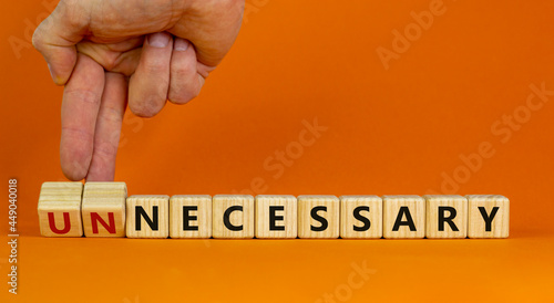 Necessary or unnecessary symbol. Businessman turns wooden cubes and changes the word Unnecessary to Necessary. Beautiful orange background, copy space. Business and necessary or unnecessary concept. photo