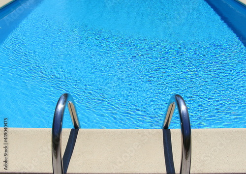 Blue water in the pool in summer. Relaxation and rest. The sun's rays are reflected in the water. Entrance to the pool with metal handrails.