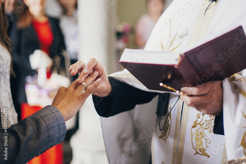 Priest putting on stylish wedding ring with feather on groom finger in during holy matrimony in church. Wedding ceremony in cathedral. Wedding rings for bride and groom