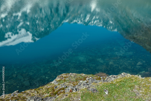 Snowy mountain reflected in clear water of glacial lake. Beautiful sunny landscape with snow-white glacier reflection in water surface of mountain lake. White snow on rock reflected in mountain lake.