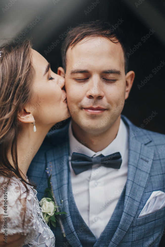 Stylish bride kissing happy groom in cheek on background of old church. Romantic moment. Provence wedding. Portrait of beautiful sensual wedding couple gently embracing in european city. Stylish bride kissing happy groom in cheek on background of old church. Romantic moment. Provence wedding. Portrait of beautiful sensual wedding couple gently embracing in european city.