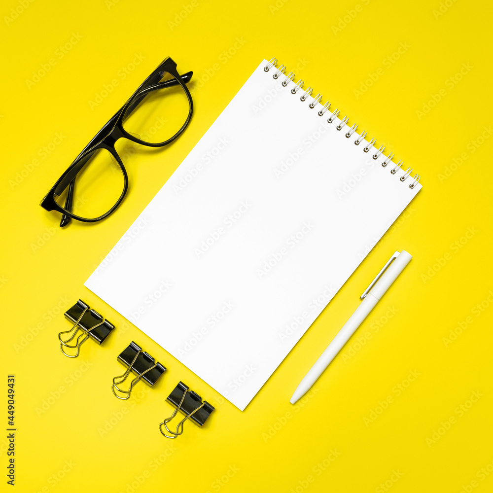 Notepad, pen, glasses and binder clips on yellow background. Flat lay, top view, copy space. Notepad, pen, glasses and binder clips on yellow background. Flat lay, top view, copy space.