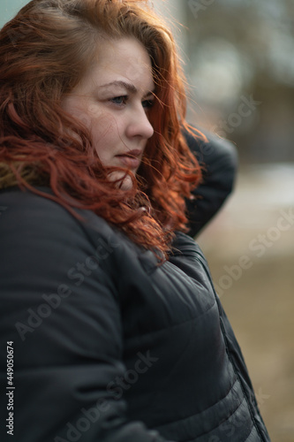 Young beautiful blue-eyed red-haired plump girl in autumn clothes outdoors.