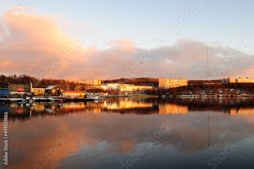 The sun sits beautifully and is reflected in the water and on houses. Northern city of Murmansk, Leninsky district. View of Lake Semenovskoye, Murmansk, Russia.