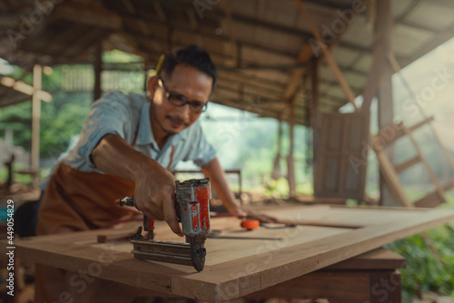 Carpenter uses a nail gun to assemble wood furniture in a factory.