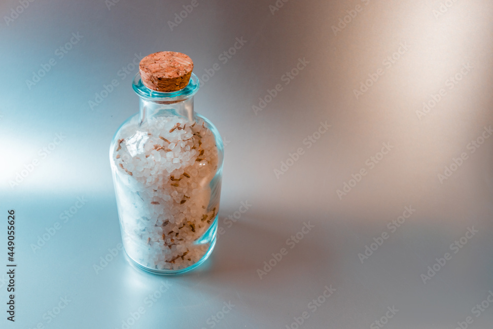 A large closed glass container with sea white salt stands against a light kitchen background. A large closed glass container with sea white salt stands against a light kitchen background.