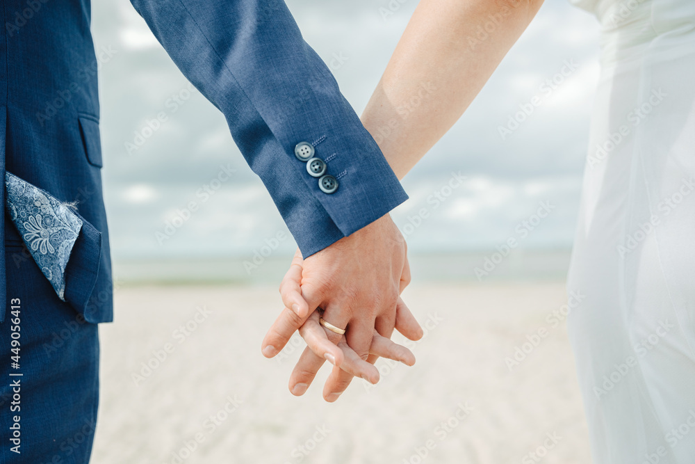 The bride and groom hold hands and walk together on the beach of the North Sea 