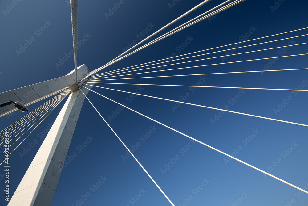 Minimalist abstract architecture shot featuring a white concrete pillar of a suspension bridge with a bunch of suspension cables against a clear blue sky Minimalist abstract architecture shot featuring a white concrete pillar of a suspension bridge with a bunch of suspension cables against a clear blue sky