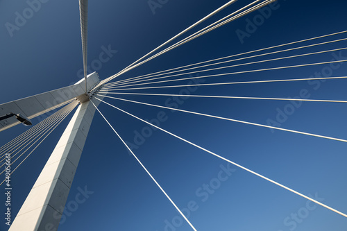 Minimalist abstract architecture shot featuring a white concrete pillar of a suspension bridge with a bunch of suspension cables against a clear blue sky