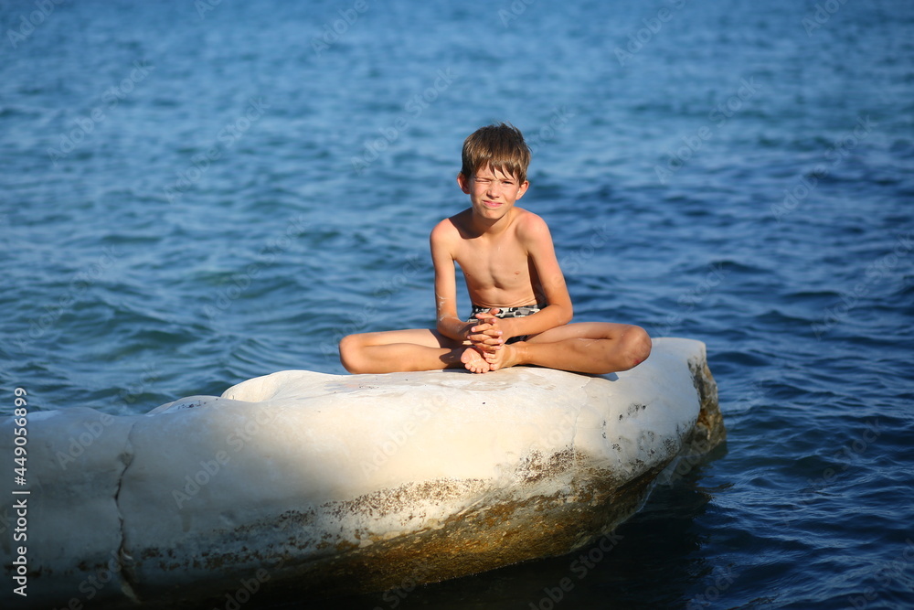 Fototapeta premium Caucasian nine year old boy sunbathing on the rocks on the cyprus seashore