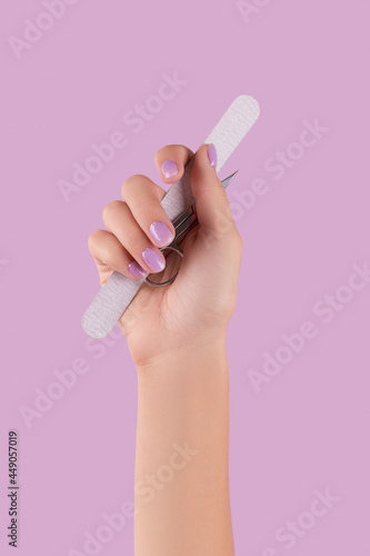 Womans hand holding manicure instrument on pastel lavender background photo