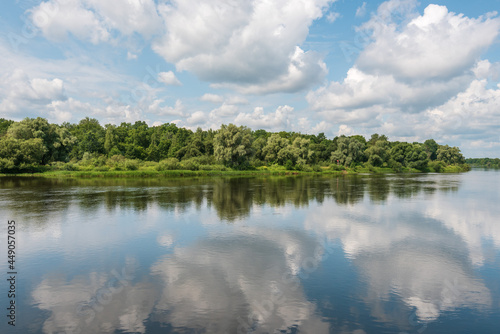 Summer landscape. Sunny day. The beautiful blue sky with clouds is reflected in the wide river. The nature of Belarus.