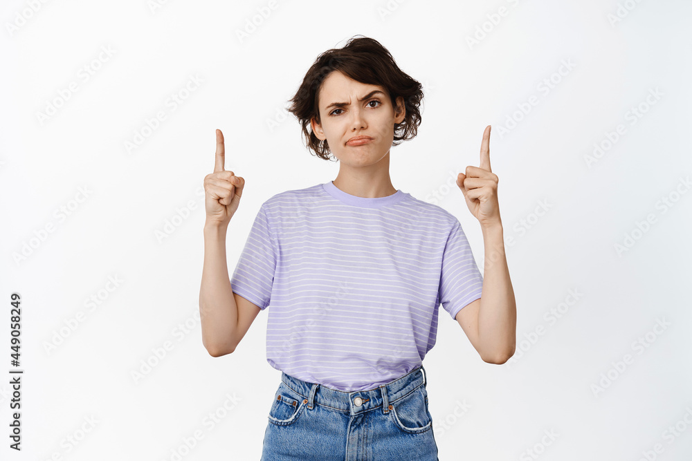 Skeptical frowning woman pointing fingers up, bad idea, complaining, doubtful about product or shop, having doubts, squinting with disbelief, white background Skeptical frowning woman pointing fingers up, bad idea, complaining, doubtful about product or shop, having doubts, squinting with disbelief, white background