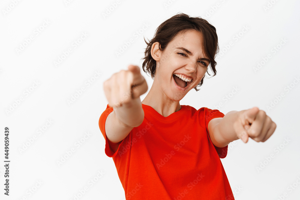 Its you congrats. Smiling cheerful girl pointing fingers at camera, congratulating, inviting you to an event, standing in red t-shirt over white background Its you congrats. Smiling cheerful girl pointing fingers at camera, congratulating, inviting you to an event, standing in red t-shirt over white background