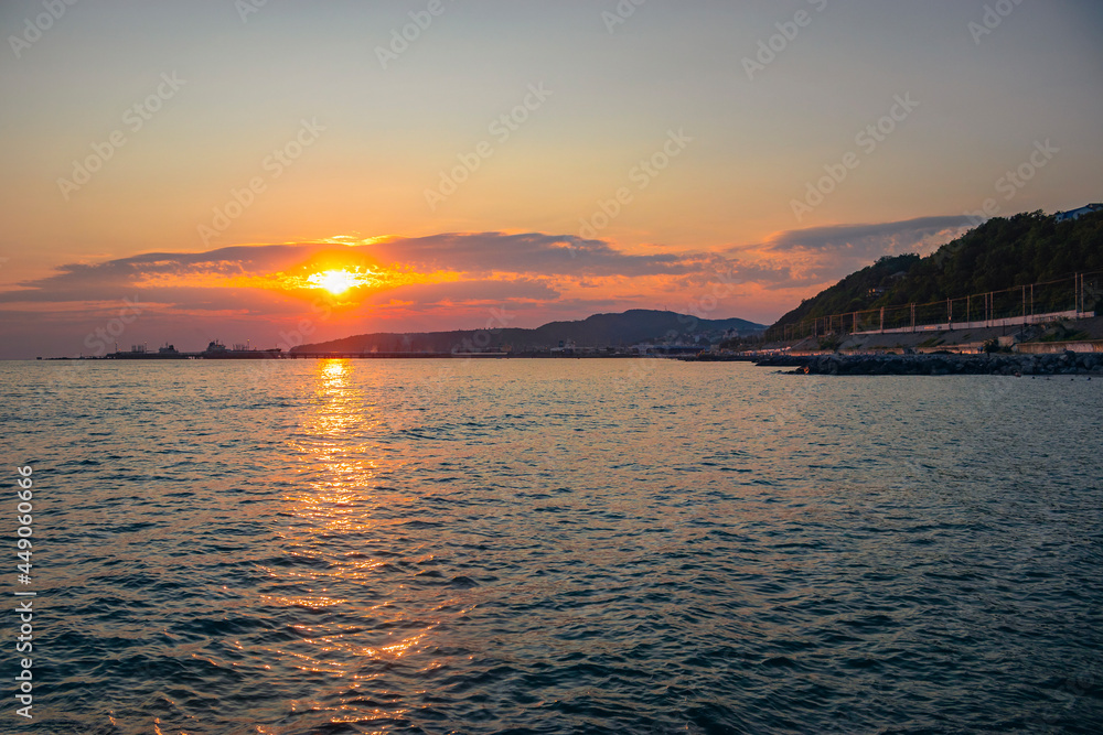 Orange sunset on the mountainous coast of the sea with ships. Beautiful sunset over the Black Sea. Evening landscape over the rocky sea coast.