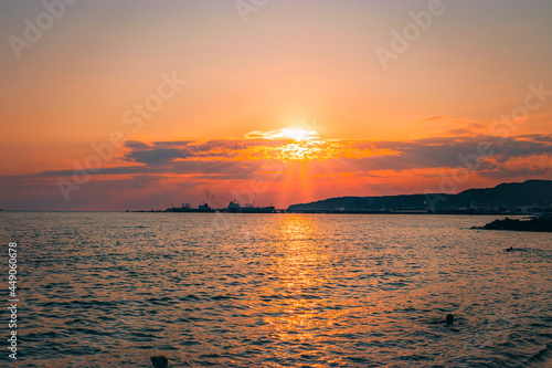 Orange sunset over the mountainous coast of the sea with ships. Beautiful sunset over the Black Sea. Evening landscape with a bright sun reflected in the sea water.