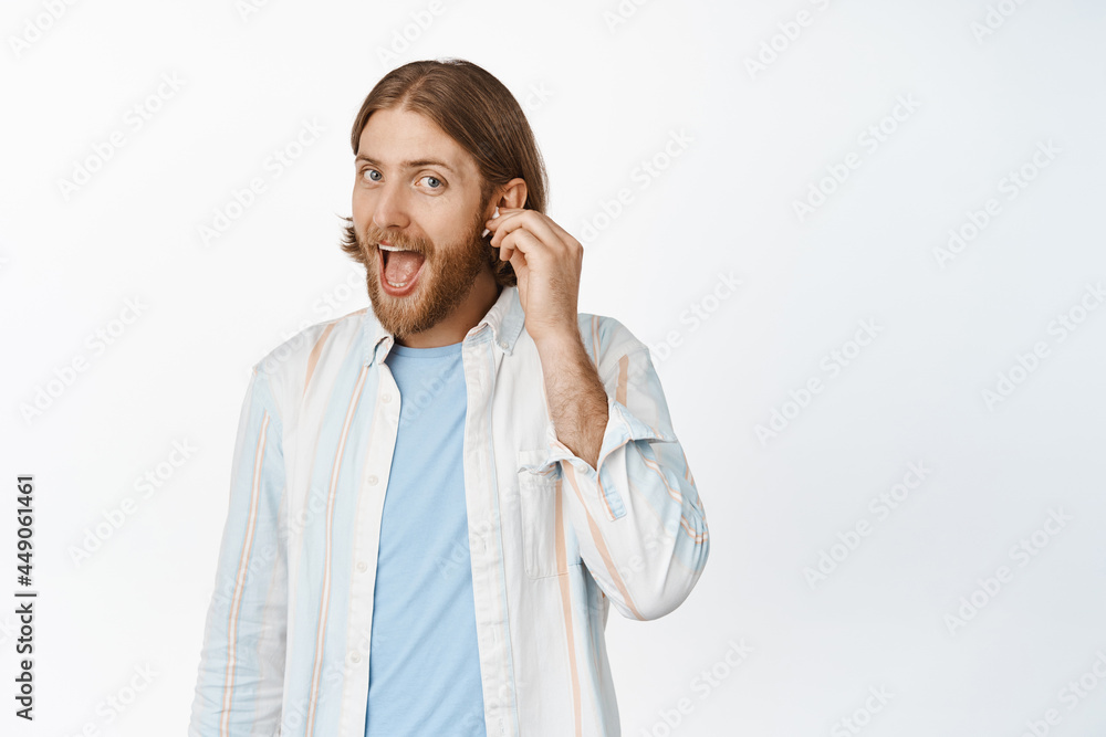 Portrait of handsome blond man put on earphone, listen music with headphones and smiling, standing against white background Portrait of handsome blond man put on earphone, listen music with headphones and smiling, standing against white background