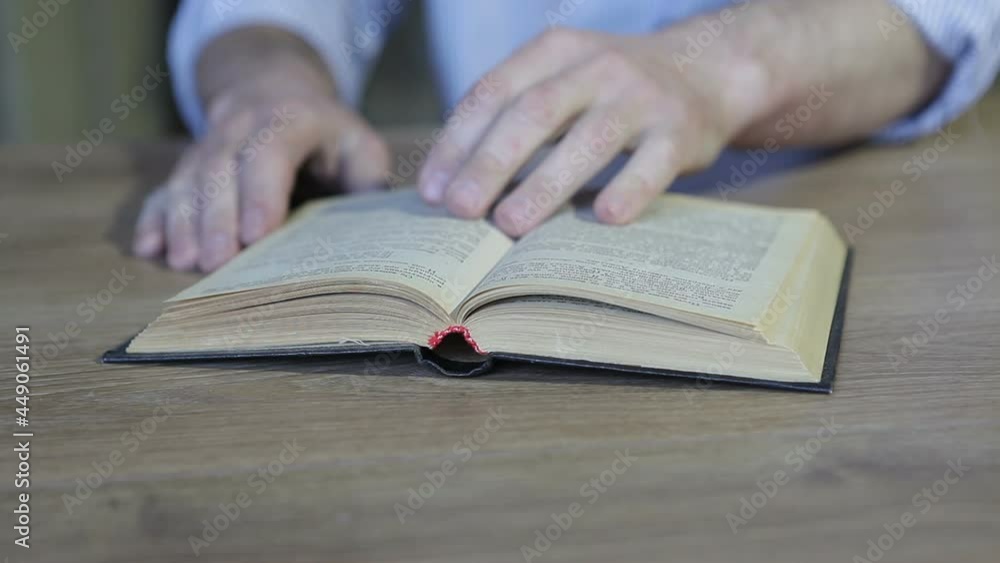 A man is reading a book at the table. The man puts his glasses on the open book. A man is reading a book at the table. The man puts his glasses on the open book.