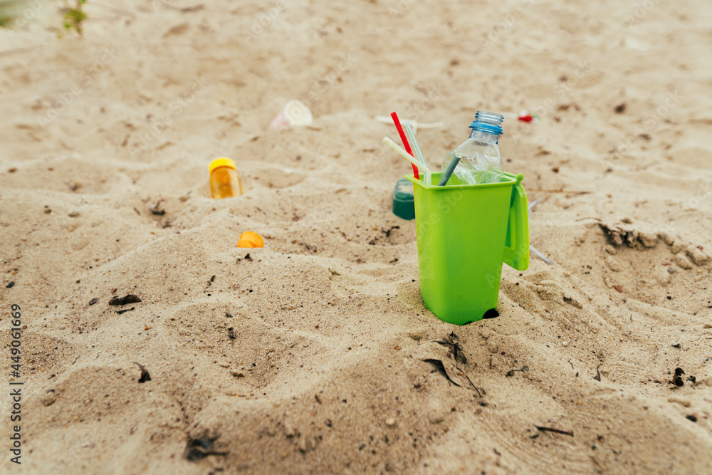 Small toy waste container on the sand beach with plastic garbage Small toy waste container on the sand beach with plastic garbage