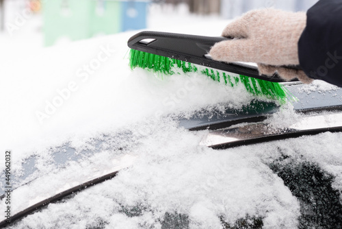 Snow removal, car in snow. Woman cleans the car from snow.