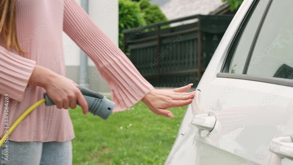 Handheld shot of a Caucasian woman putting a charging plug or charger in a white electric car Handheld shot of a Caucasian woman putting a charging plug or charger in a white electric car