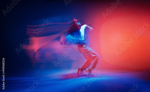 Fototapeta Naklejka Na Ścianę i Meble -  Dancing female standing on tiptoe in colourful neon studio light. Long exposure. Contemporary hip hop dance