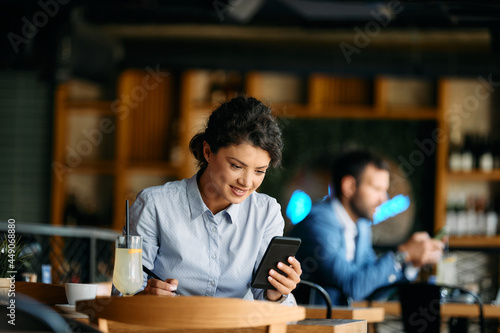 Young smiling businesswoman reads text message on smart phone in cafe.